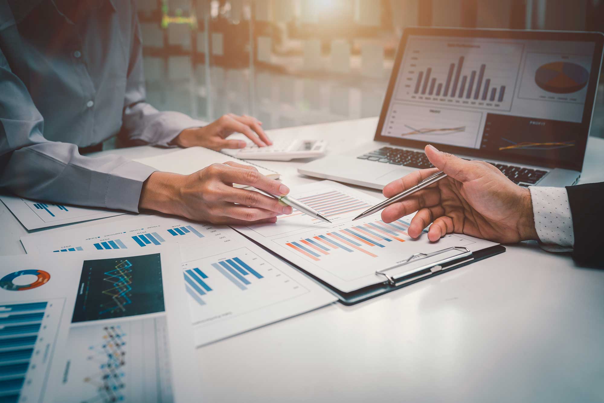 Two professionals review financial charts and graphs together at a desk.